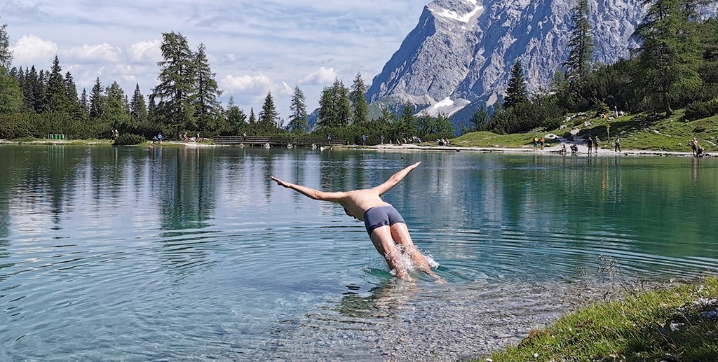 DMC in Alps – A man diving into a crystal-clear Alpine lake, surrounded by towering snow-