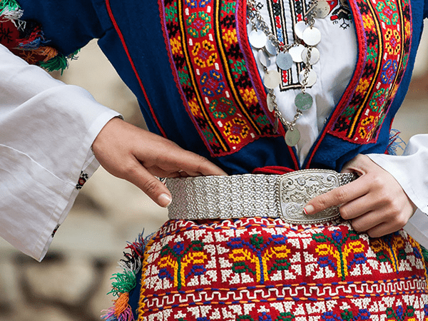  Traditional Bulgarian attire showcased by a DMC in Bulgaria, featuring intricate embroidery, vibrant patterns, and a detailed silver belt.