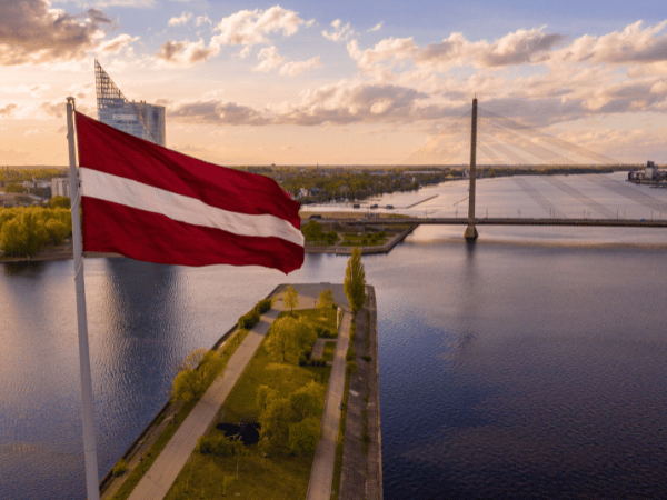 DMC in Latvia – Latvian flag waving over the Daugava River at sunset in Riga.