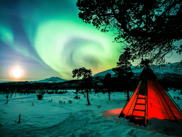 DMC in Sweden – Red tent glowing under the aurora borealis in Swedish Lapland’s winter wonderland.